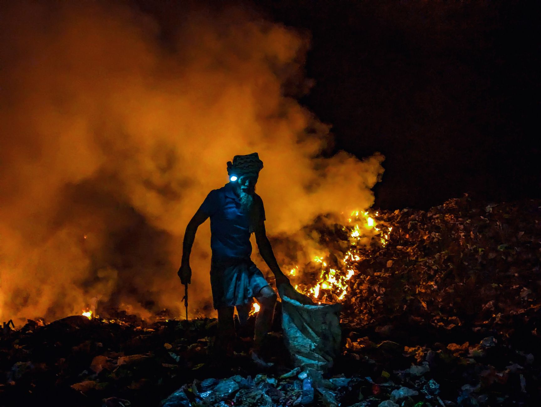 silhouette of worker amidst burning garbage at night